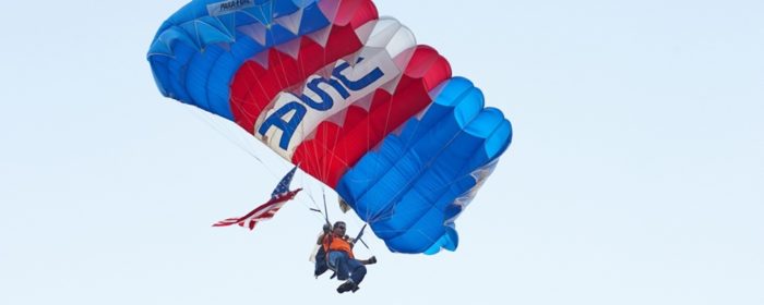 Skydiver with parachute holds US flag.