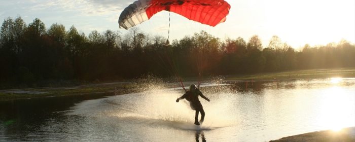 Skydiver glides across a lake with parachute.