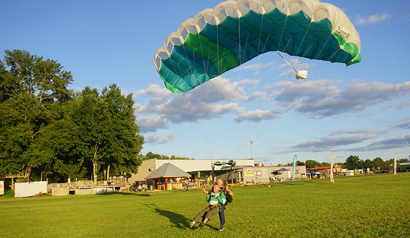 Tandem skydiver landing in a green field.