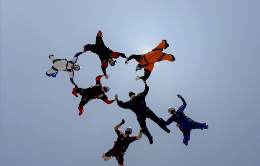 Group of skydivers form a ring in the air.
