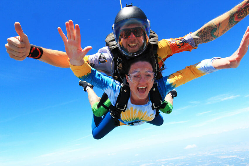 Tandem skydiving instructor giving thumbs up during freefall with new skydiver.