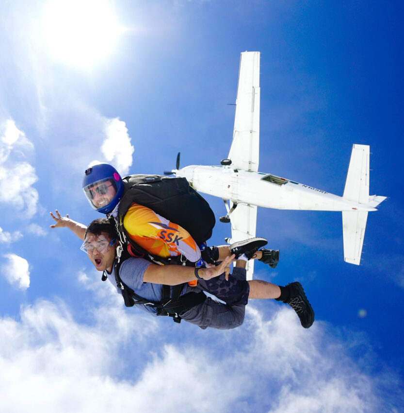 Tandem skydivers below the plane after jumping with clouds in the background over NJ.